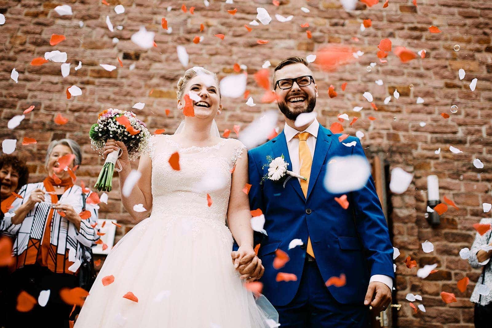Ein frisch verheiratetes Brautpaar verlässt lachend den Trauraum im Kloster Landscheid und wird von der Hochzeitsgesellschaft mit Blumen beworfen.