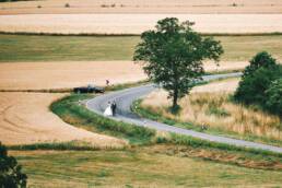 Landschaft mit serpentinenförmiger Straße mitten im Sommer, ein Brautpaar geht die Straße entlang