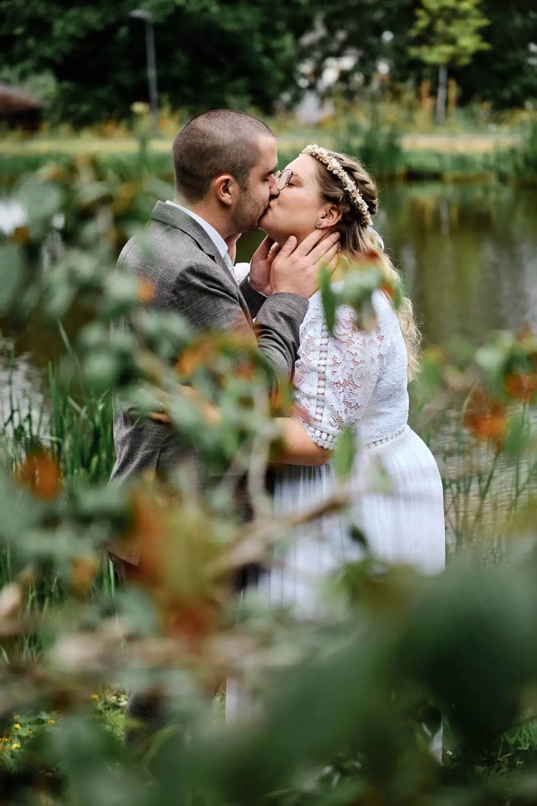 Eine romantische Aufnahme, das Brautpaar küsst sich liebevoll und werden dabei von Blättern im Vordergrund eingerahmt.
