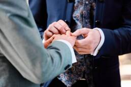 Zwei zärtliche Hände tauschen Eheringe aus, der Bräutigam schiebt sanft den Ring über den Finger seines künftigen Ehemannes.