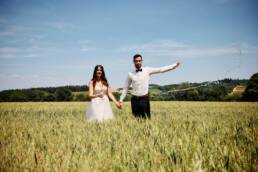 Eine Momentaufnahme, das Brautpaar steht im Weizenfeld und schüttet den Sekt in die Luft.