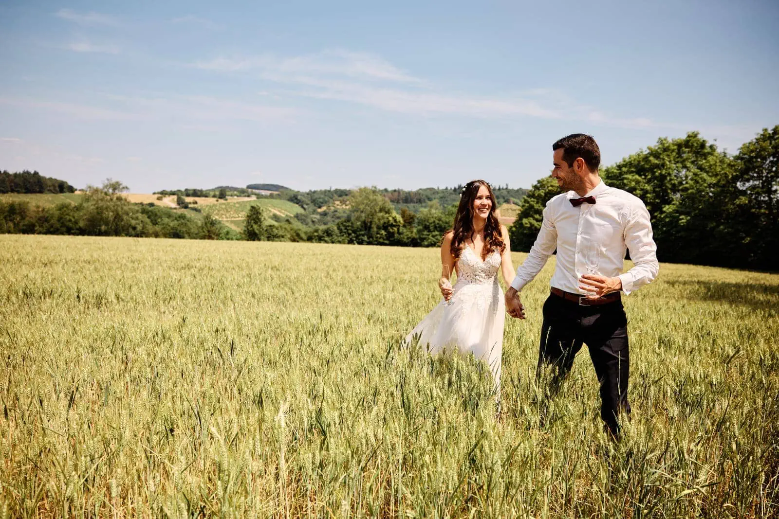 Das Brautpaar geht Händchenhaltend durch das Weizenfeld.